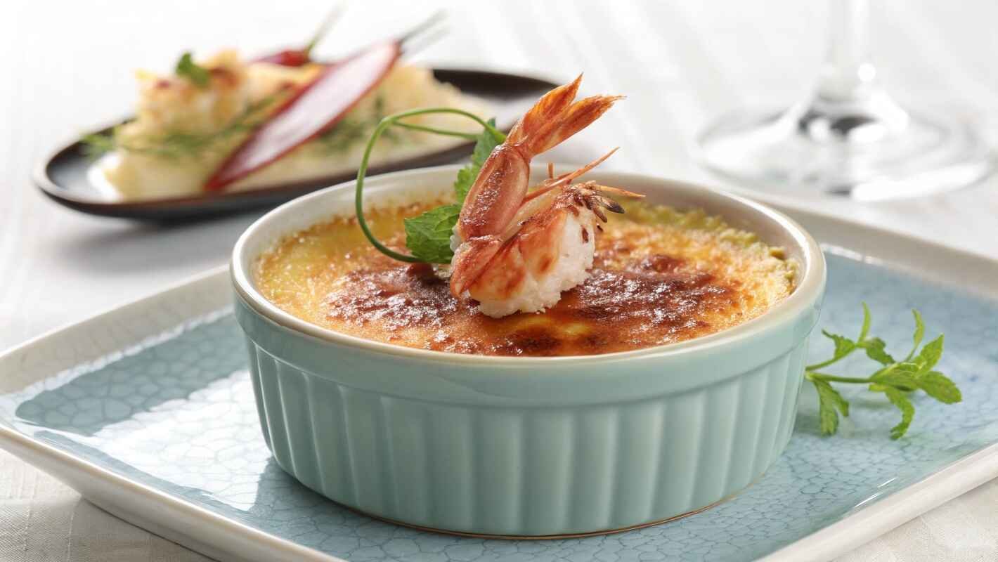 Crab Brûlée Served In An Elegant Light Blue Ramekin, Its Surface Perfectly Caramelized To A Deep Golden Brown Crust.